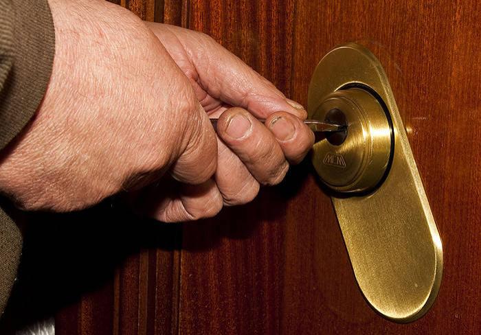 Un hombre intenta forzar la cerradura de una puerta con una herramienta.